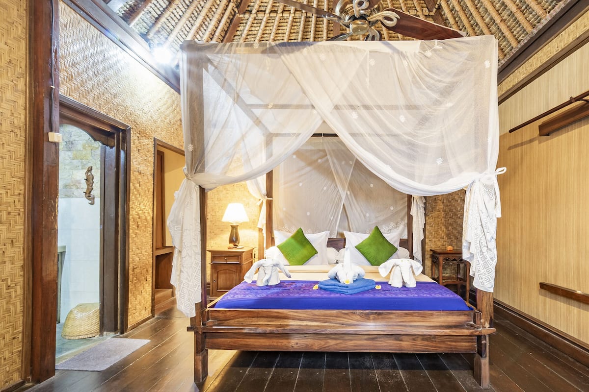 A traditional wooden bed with a canopy, green pillows, and white towels.