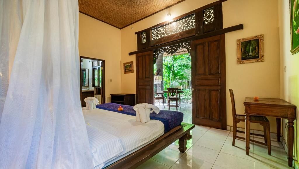 A room with a bed, a desk, and a chair. There is a door leading to an outdoor area.