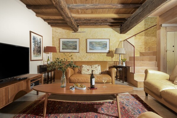 A cozy living room with a wooden coffee table, a sofa, and a TV. There are framed pictures on the wall, a staircase, and a door. - The Manger, Westwater, Axminster, Devon (Axminster)