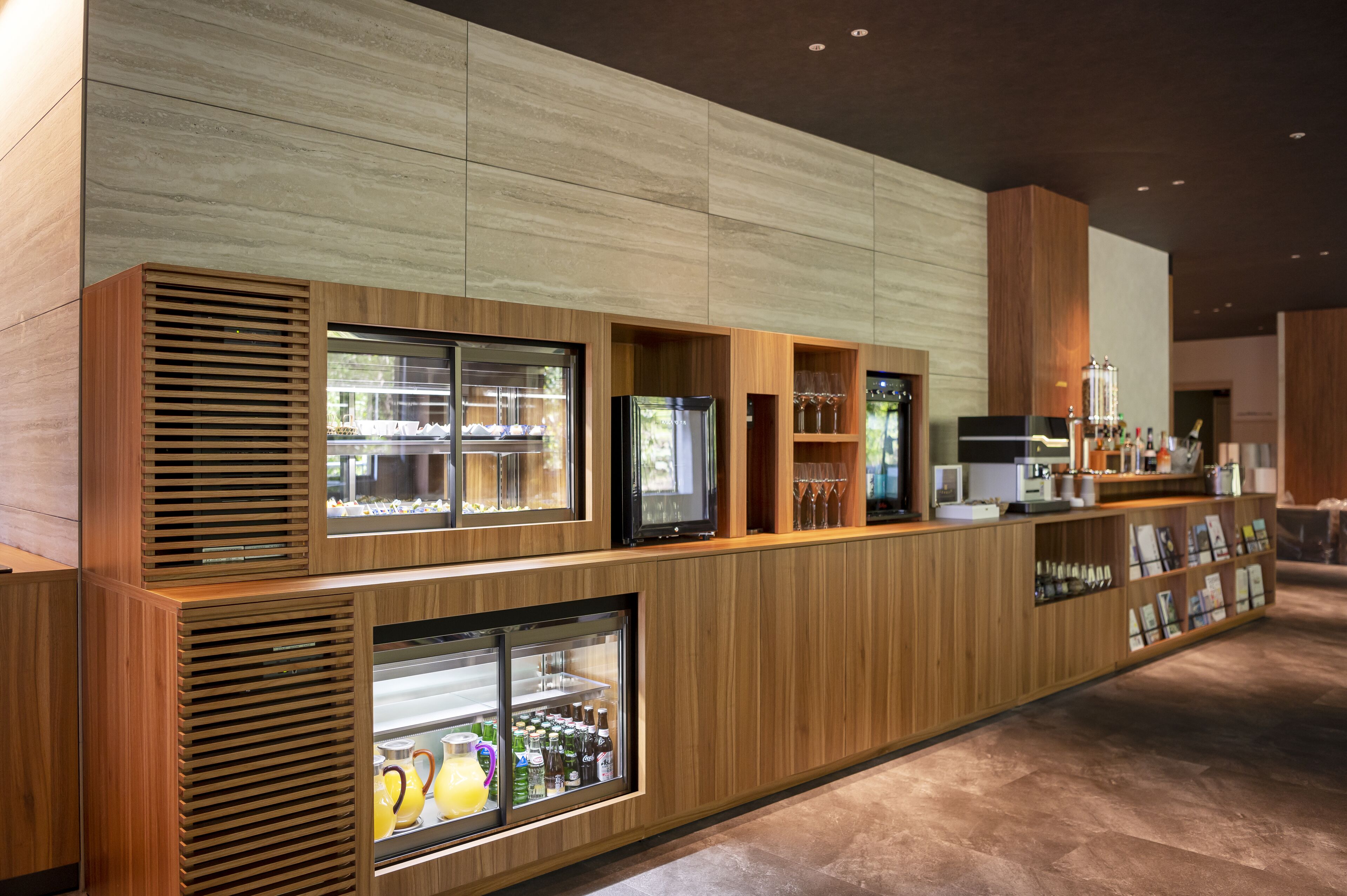 Un área de bar moderna con paneles de madera, vitrinas refrigeradas y un expositor de vidrio con bebidas.