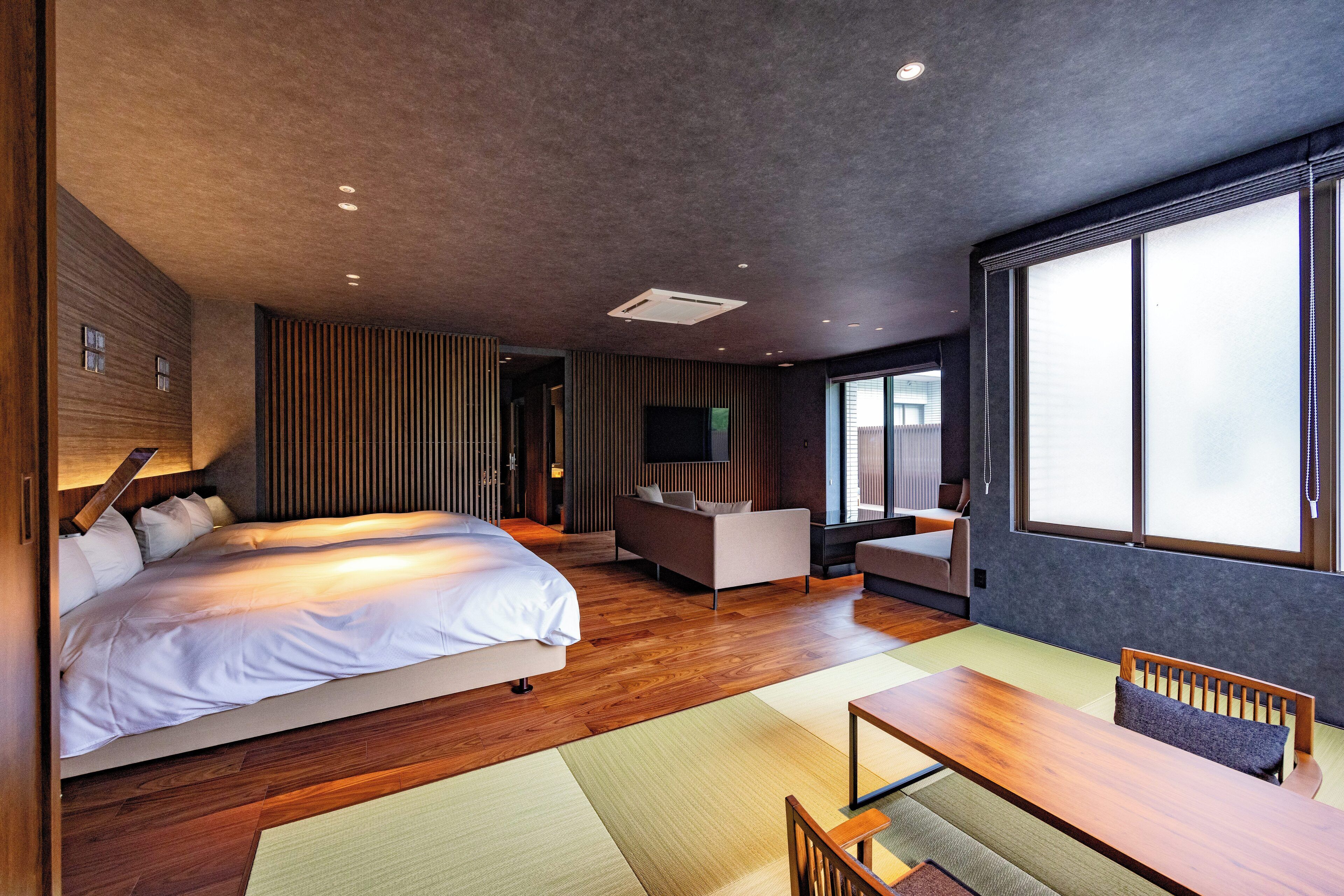 A modern hotel room with a large bed, a sofa, a dining table, and a TV.