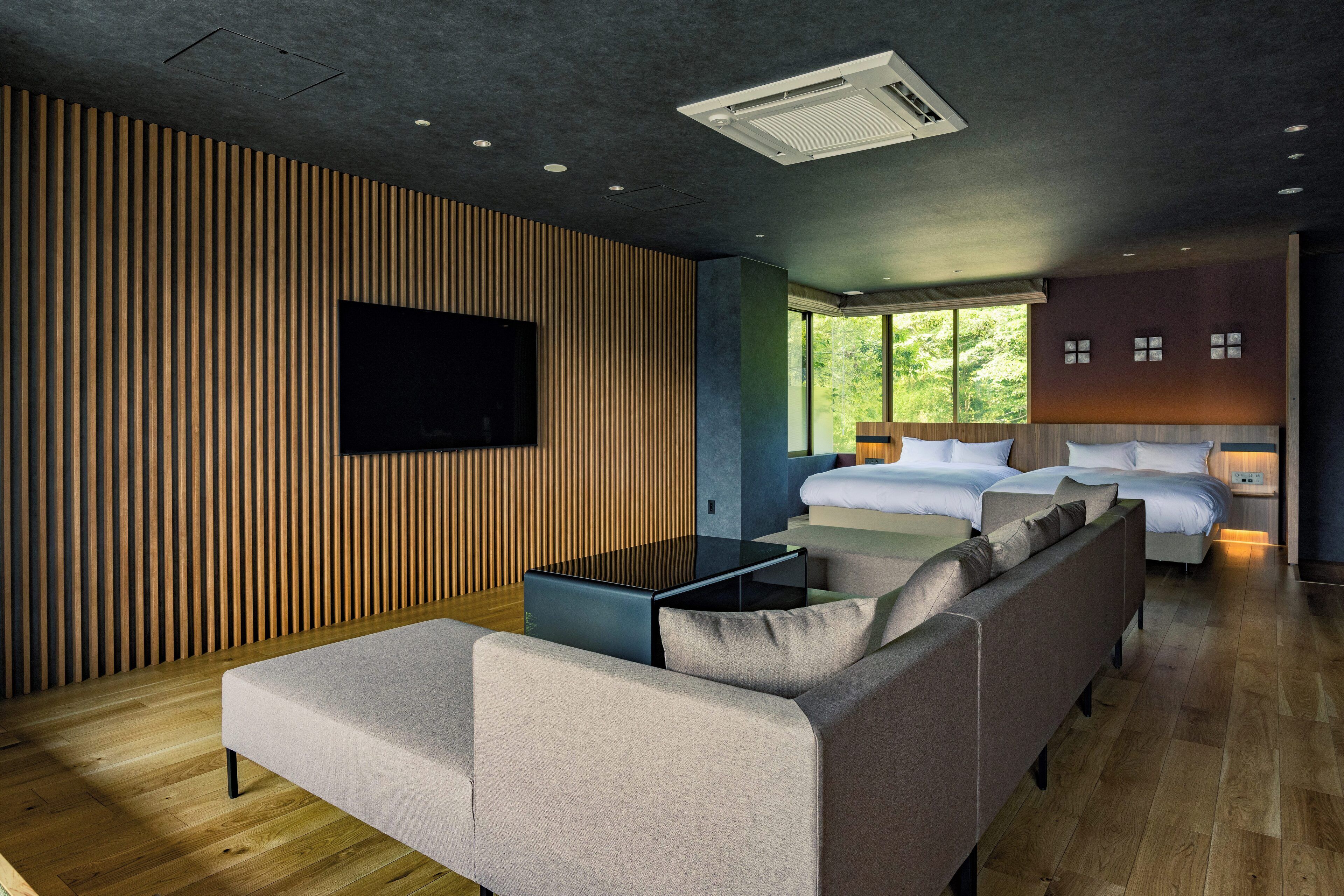 A modern hotel room with a sofa, a flat-screen TV, a bedside table, and a bed with a headboard.