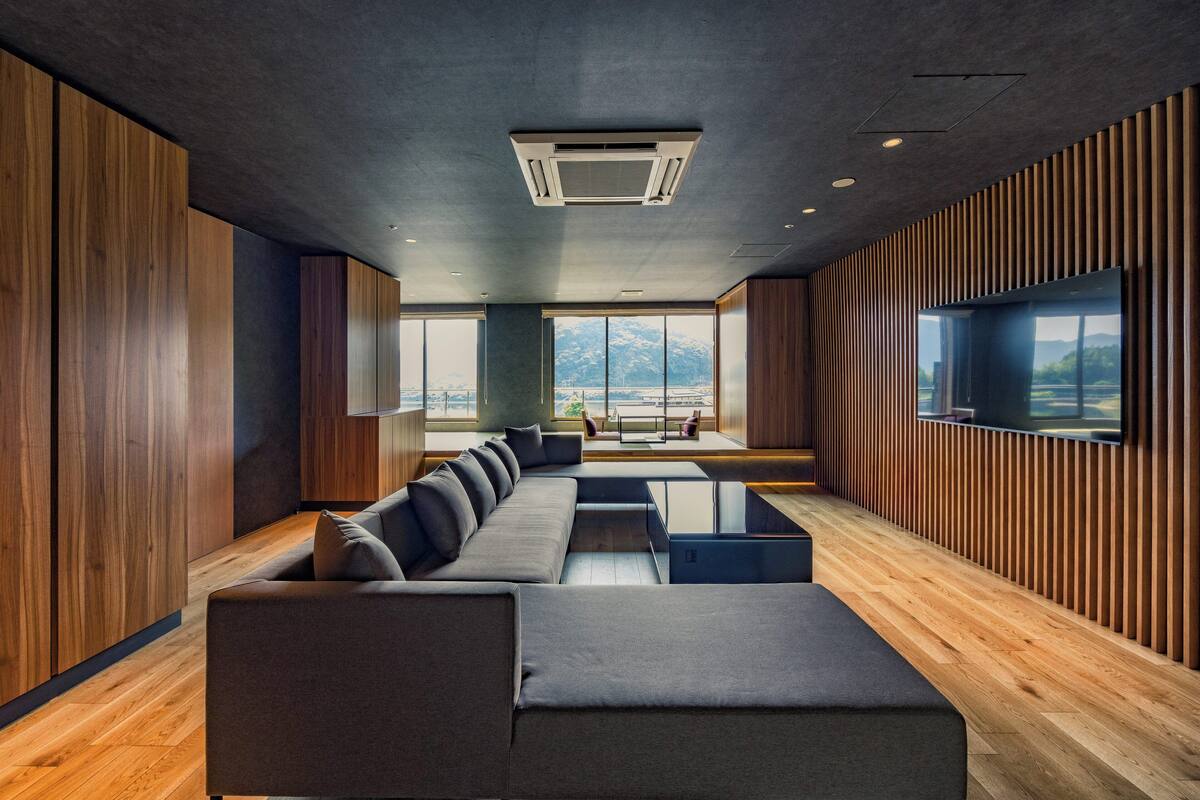 A modern interior with a large sectional sofa, wooden panel walls, and a large window offering a view of mountains.