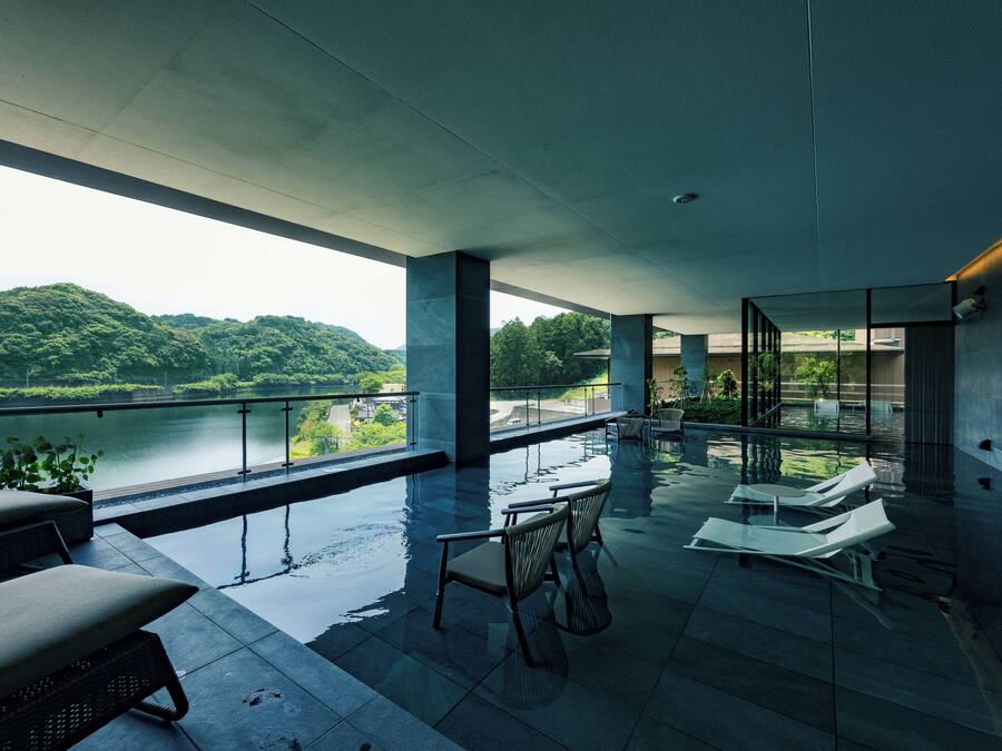 A modern indoor pool area with lounge chairs and a view of a lake and hills.