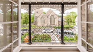 Uitzicht vanuit een raam met metalen hekwerk, over een straat met auto's en een kerk met gevel van natuursteen.