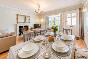 Un coin repas avec une table dressée pour quatre personnes, une cheminée, un canapé et un téléviseur.