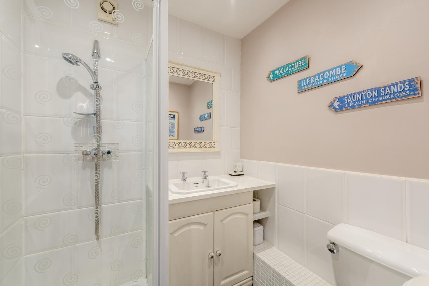 A bathroom with a shower, sink, toilet, and decorative signs on the wall.