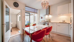 Een moderne keuken met een eettafel en rode stoelen, een klok aan de muur en uitzicht op buiten.