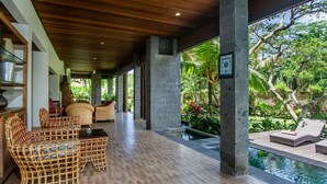 Uma área externa coberta com móveis de vime, piscina e vegetação exuberante.