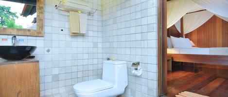 A bathroom with a toilet, sink, and a bed with a canopy.