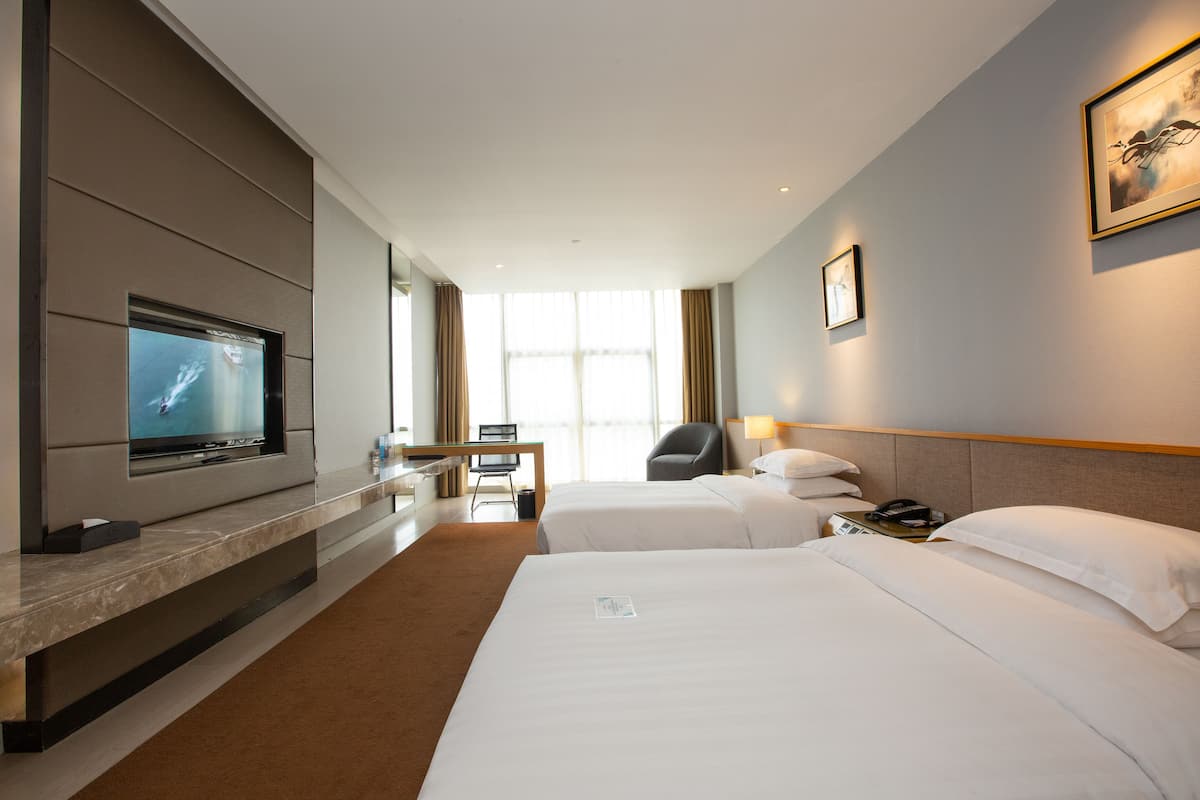 Habitación de hotel con televisión de pantalla plana, dos camas, un escritorio y una silla.