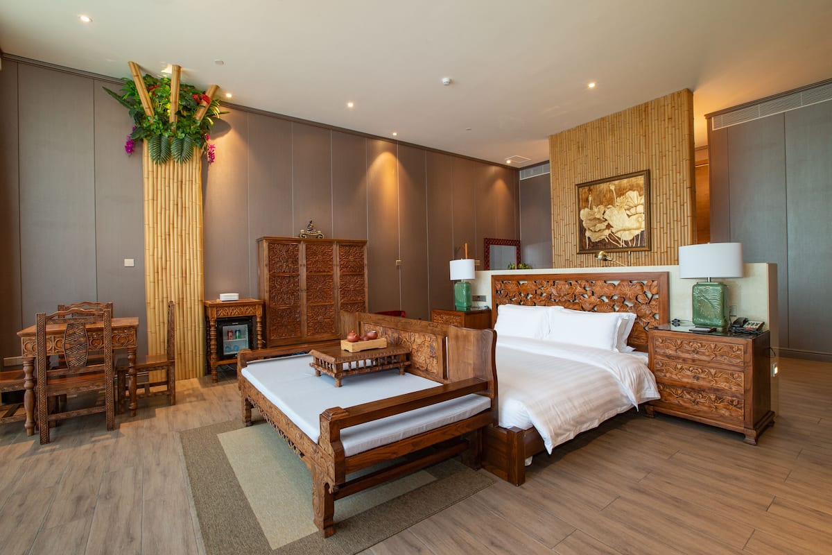 Un dormitorio espacioso con una cama grande, muebles de madera, un muro decorativo y una pequeña mesa con un florero.