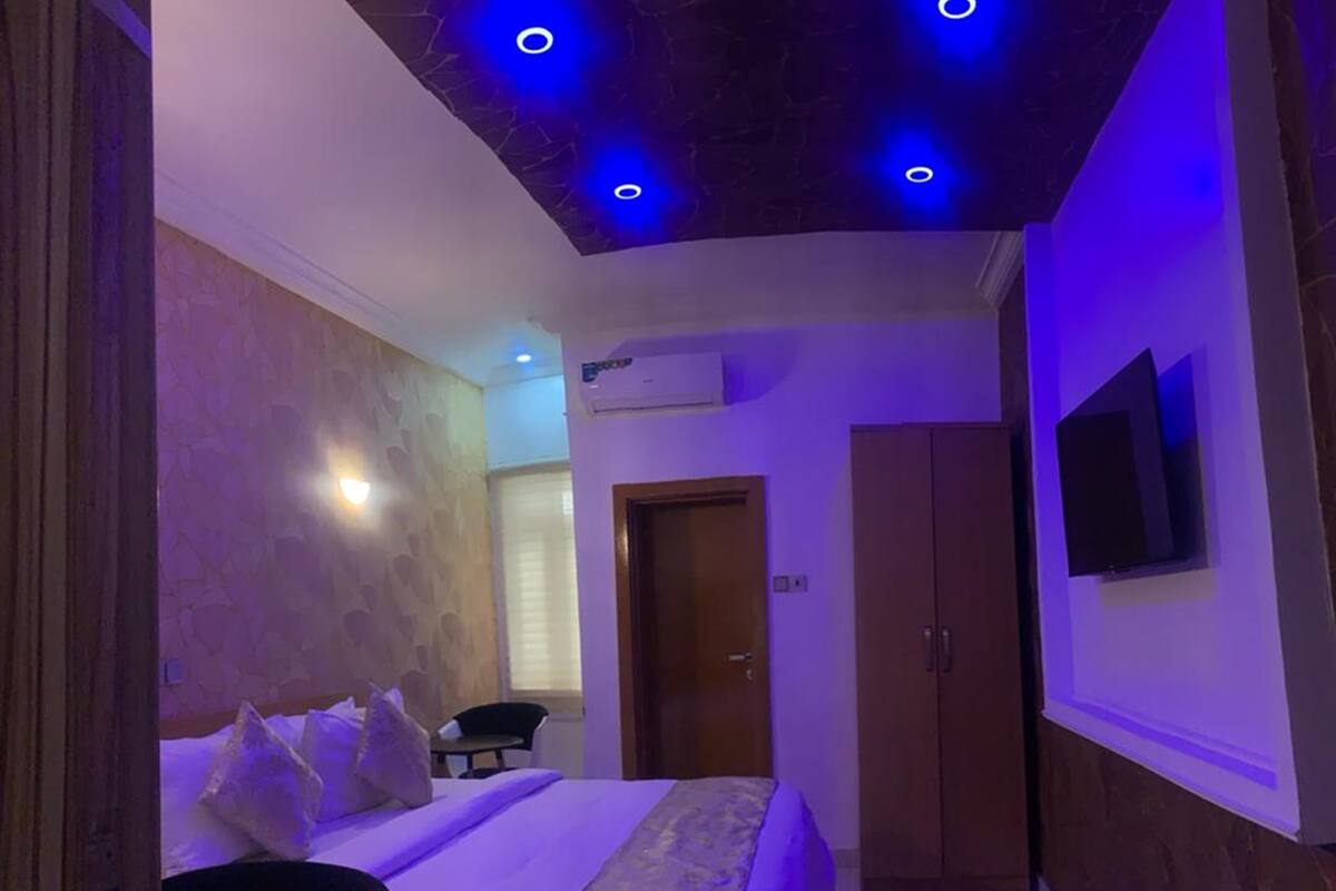 A bedroom with a bed, a wardrobe, a television on the wall, and a ceiling with recessed lighting.