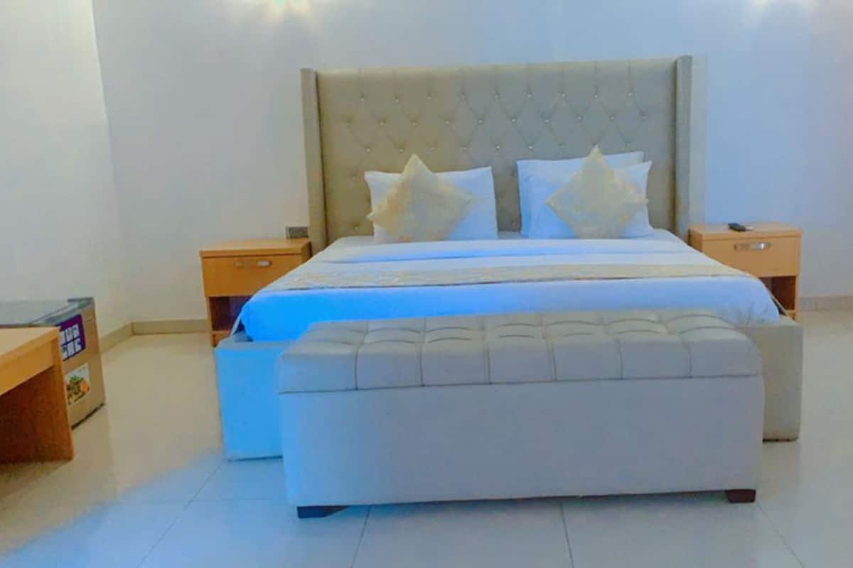 A bedroom with a large bed, two bedside tables, a nightstand, a bench, and a wardrobe.
