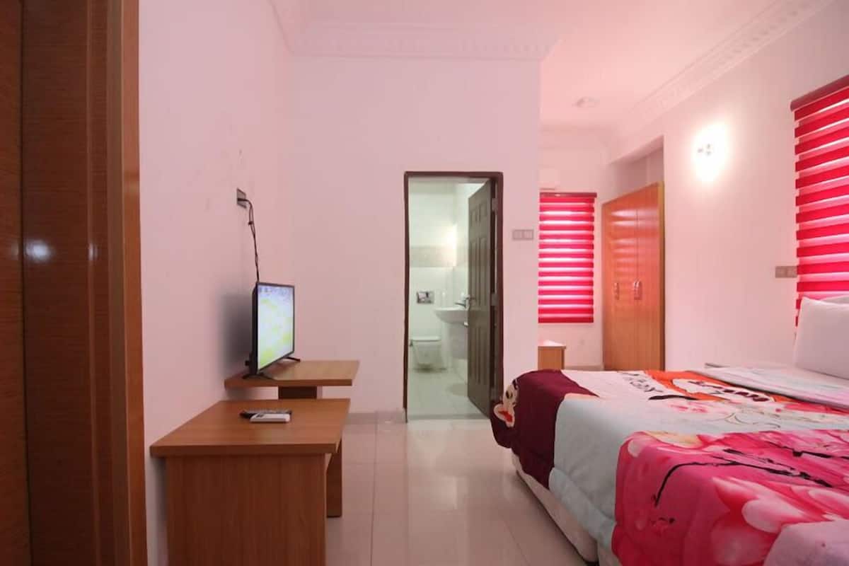 A hotel room with a bed, a desk with a computer, a wardrobe, and a bathroom visible through an open door.