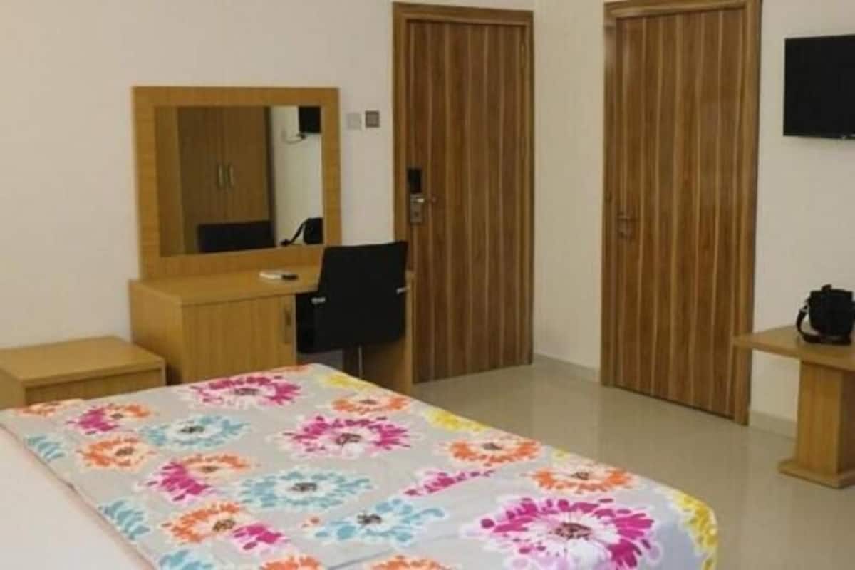 A hotel room with a bed, a desk, a chair, a mirror, and two wooden doors.