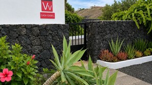 A modern building with a stone wall, a black gate, and various plants. - Wonderful views of the sea and the volcanoes. Casa Isabel  (Tías)