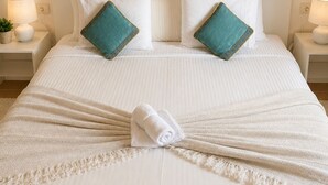 A neatly made bed with white linens and two teal pillows, a white throw blanket, and a rolled towel. - Wonderful views of the sea and the volcanoes. Casa Isabel  (Tías)