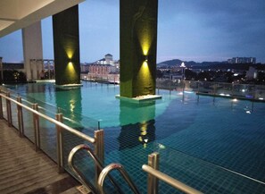 An indoor infinity pool with clear glass railings, large pillars, and city views at dusk. - Elegant Cube Soho One South (Seri Kembangan)