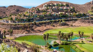A hillside residential area with modern houses, a golf course, and a body of water.