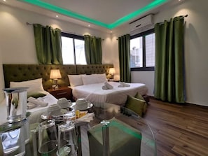 A hotel room with a large bed, two bedside tables, a desk, and a chair. There are curtains, a window, and an air conditioning unit.