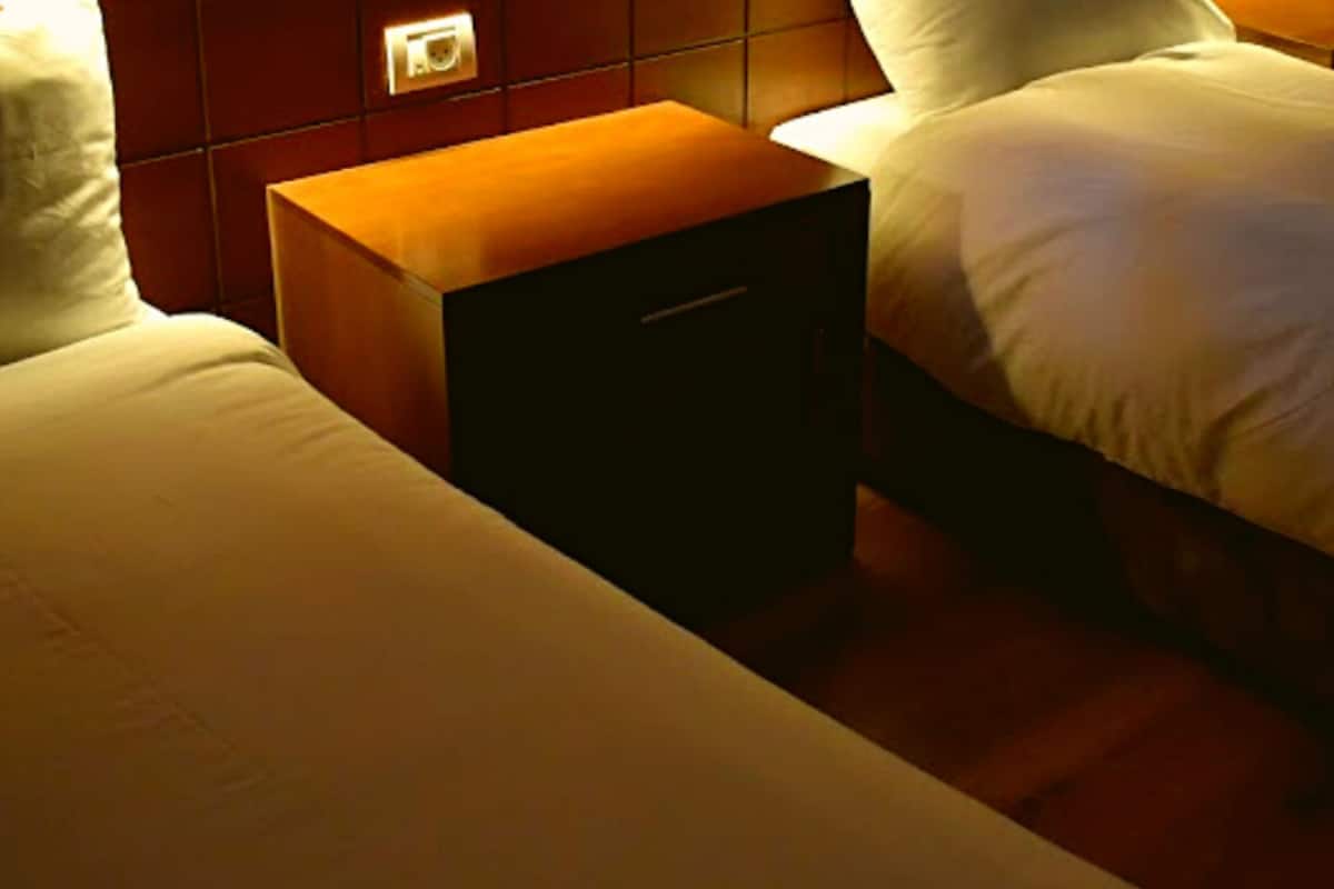 A hotel room with two beds, a nightstand, and a wall-mounted light fixture.