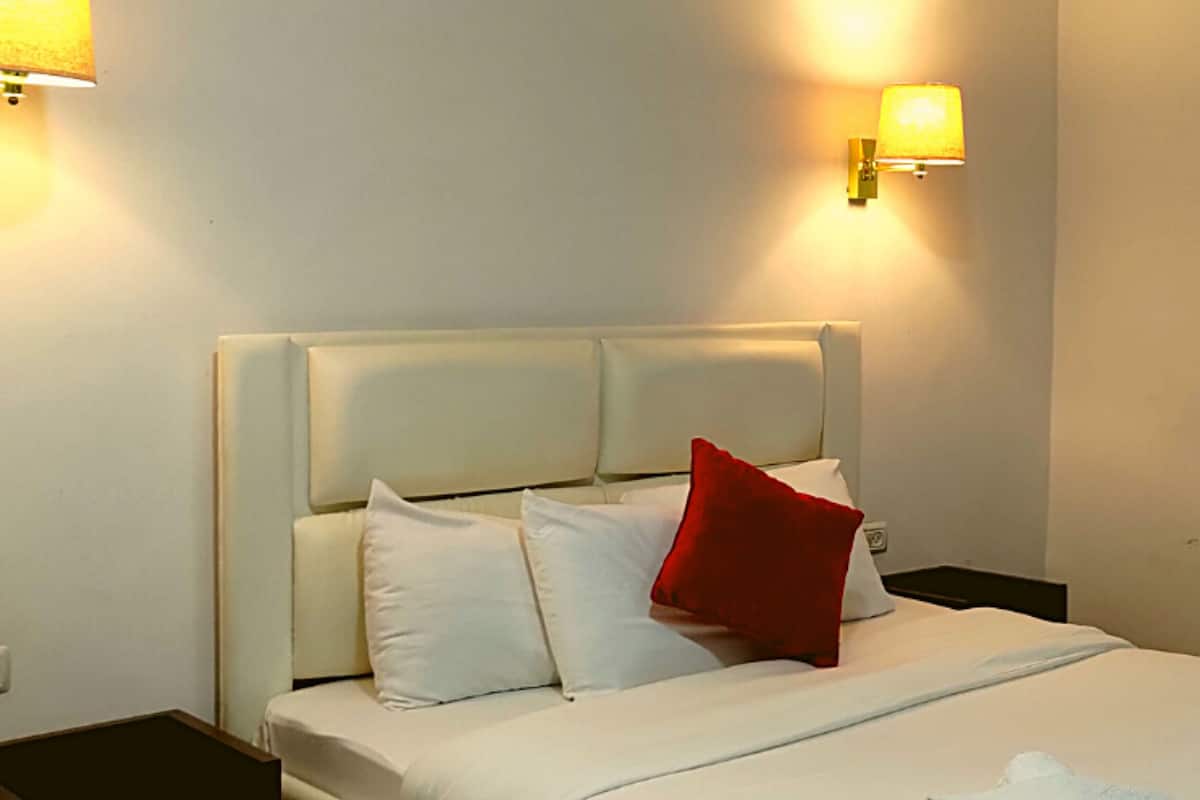 A hotel room with a bed, pillows, a nightstand, and wall-mounted lamps.