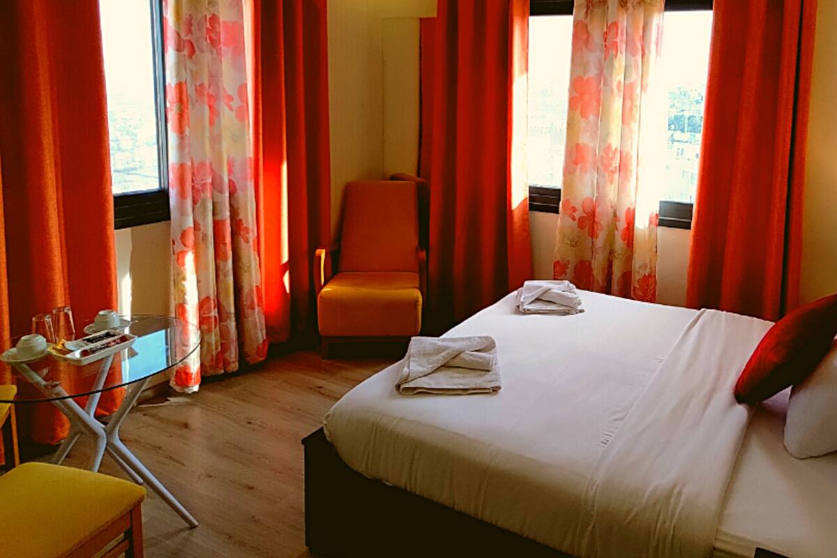 A hotel room with a bed, a chair, a table with a lamp, and curtains.