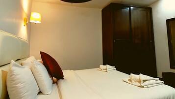 A hotel room with a bed, pillows, a wardrobe, and a wall-mounted light.