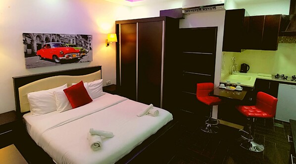 A hotel room with a bed, a desk with a chair, a sink, and a mirror.