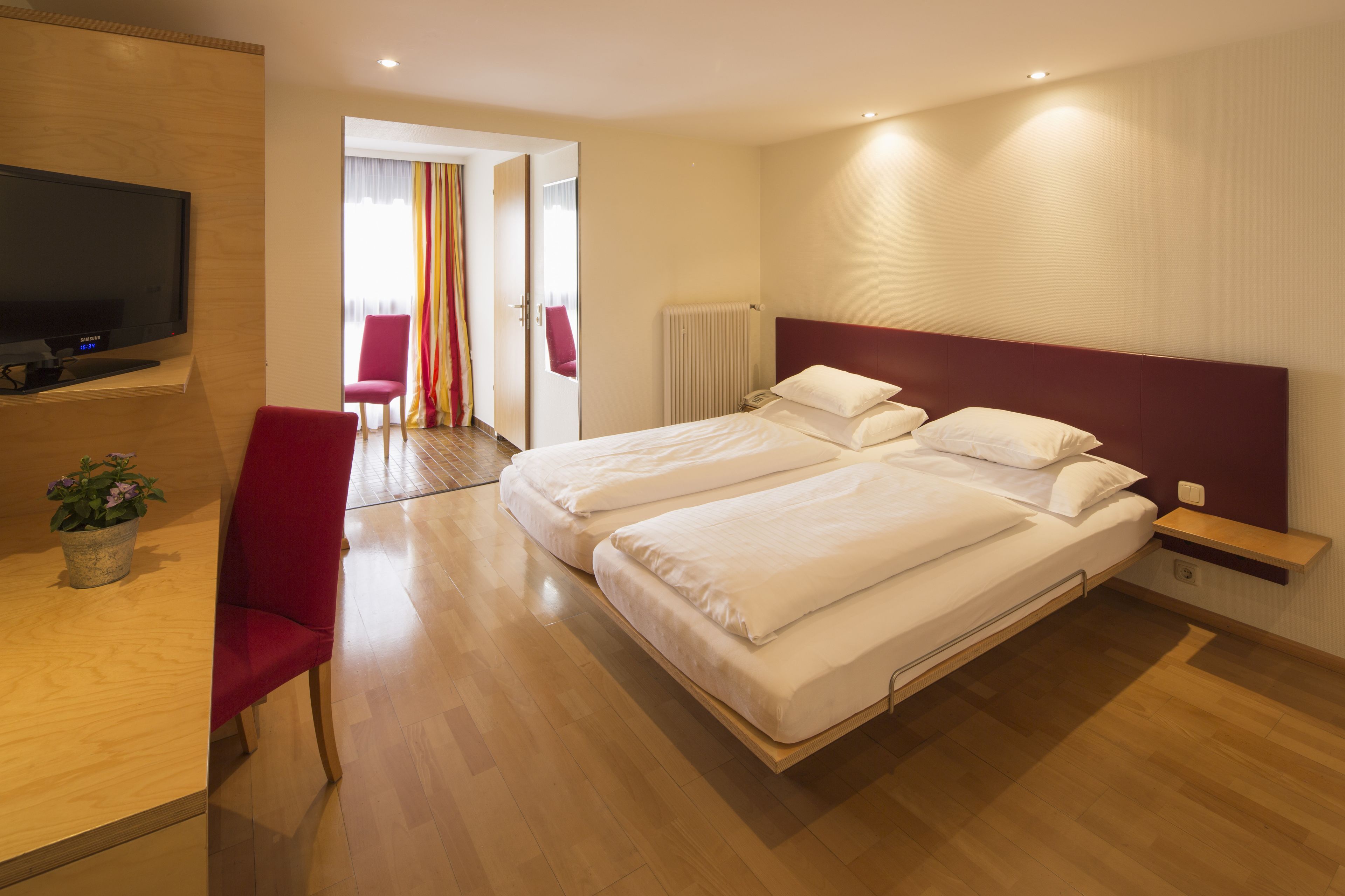 Habitación de hotel con dos camas, un televisor, un escritorio con una silla y una planta en maceta.