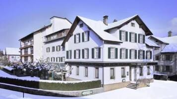 A large, multi-story building with a symmetrical facade, multiple windows, and a snow-covered roof.