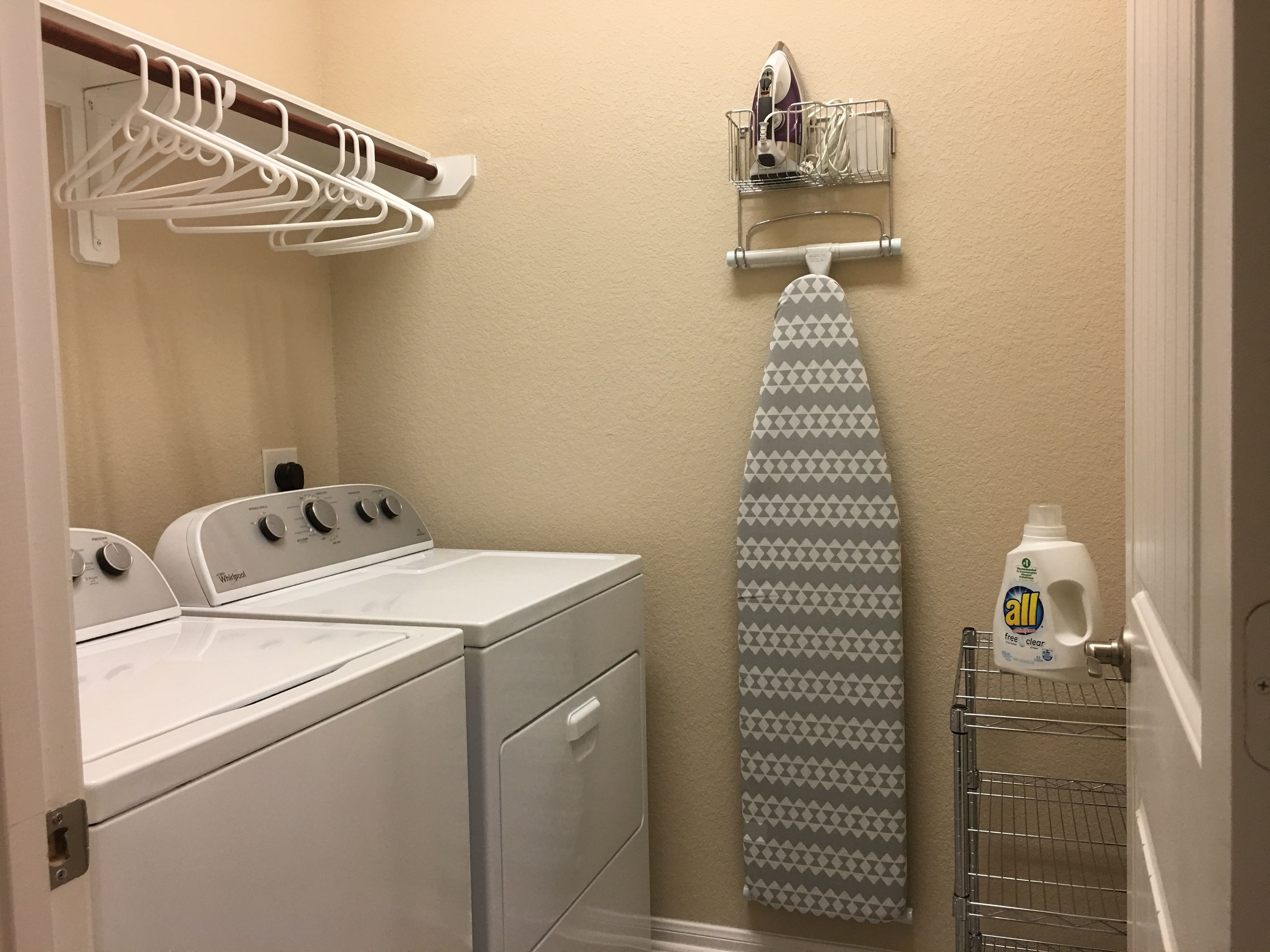 A laundry room with a washer and dryer, a drying rack, and a hanging iron.