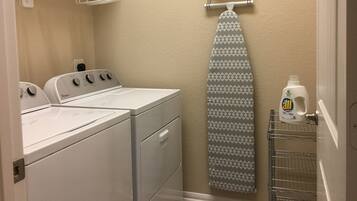 A laundry room with a washer and dryer, a drying rack, and a hanging iron.