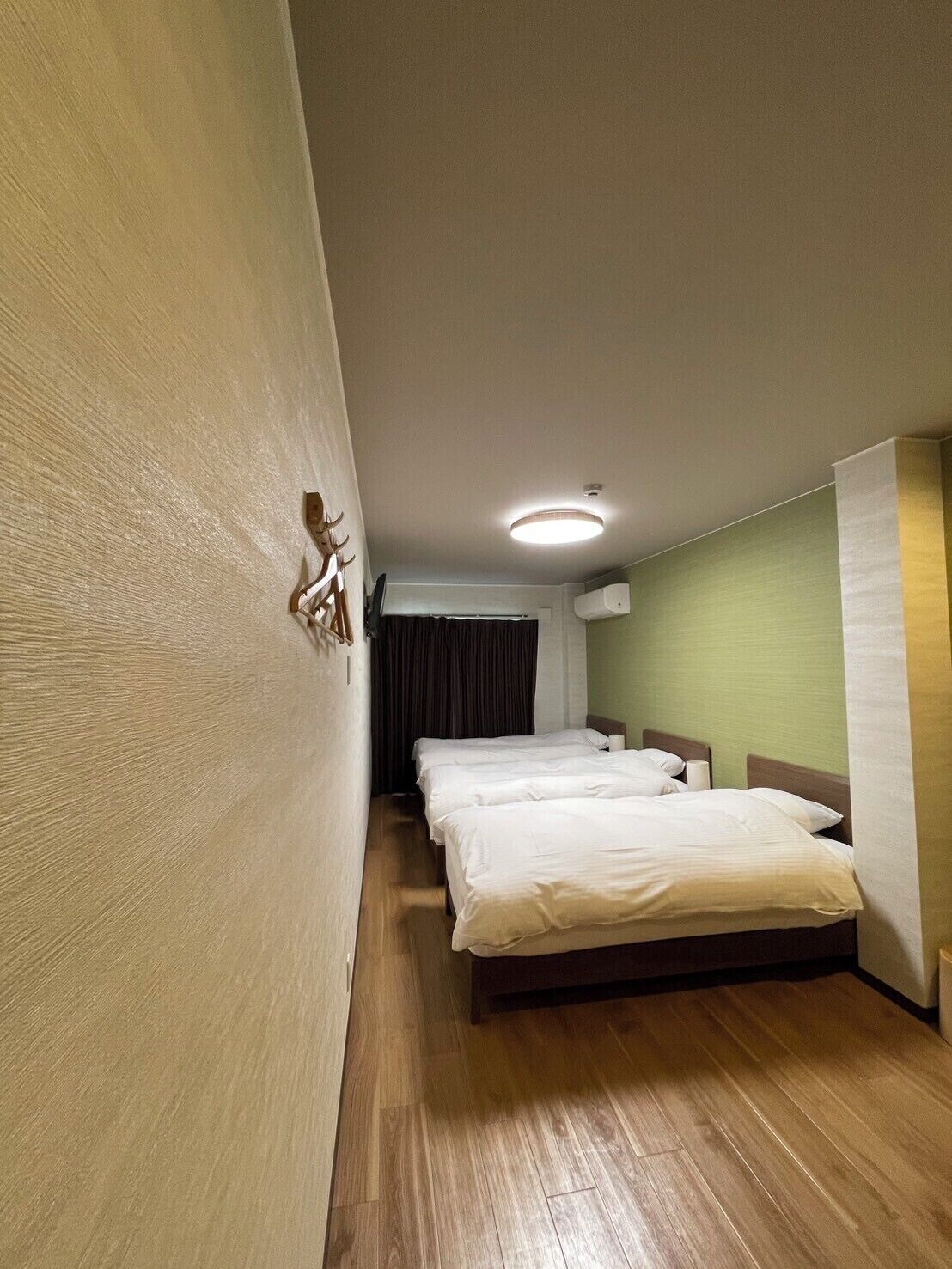 A hotel room with two beds, a wooden floor, a ceiling light, and a window with curtains.