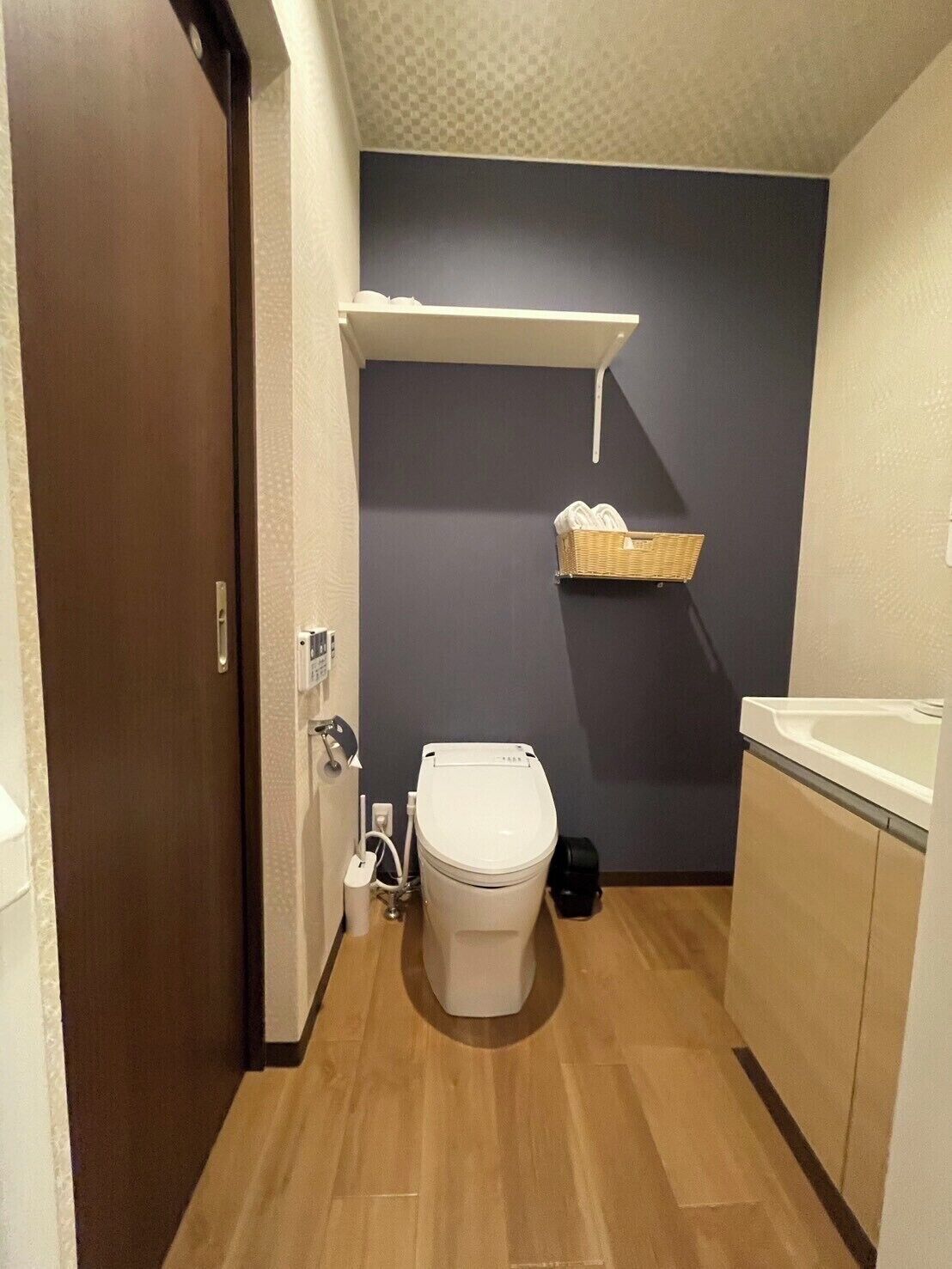 A compact bathroom with a toilet, a small shelf with towels, and a wooden floor.