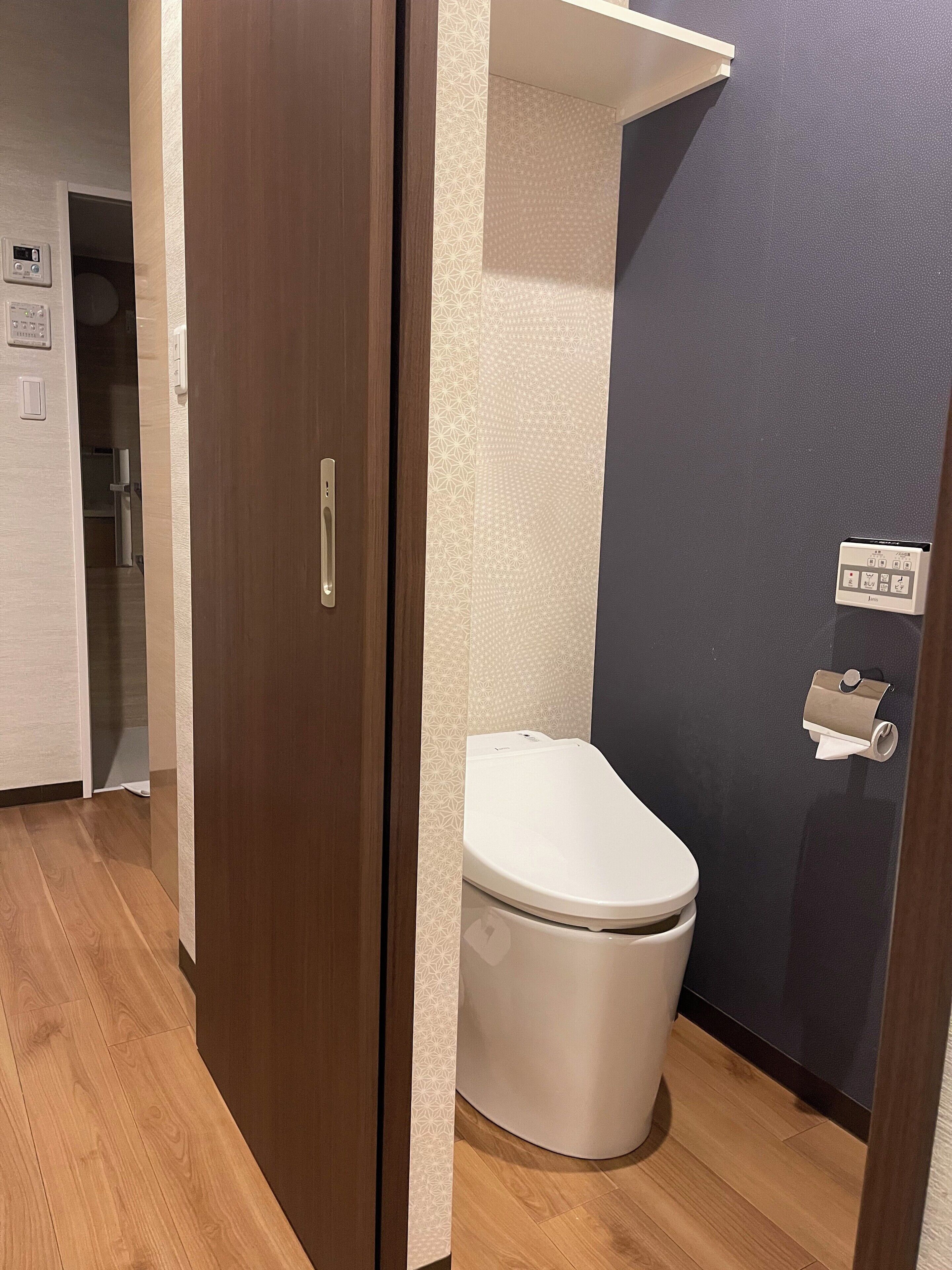 Une salle de bain moderne équipée de toilettes, d’un distributeur de serviettes et d’un porte-rouleau de papier toilette fixé au mur.