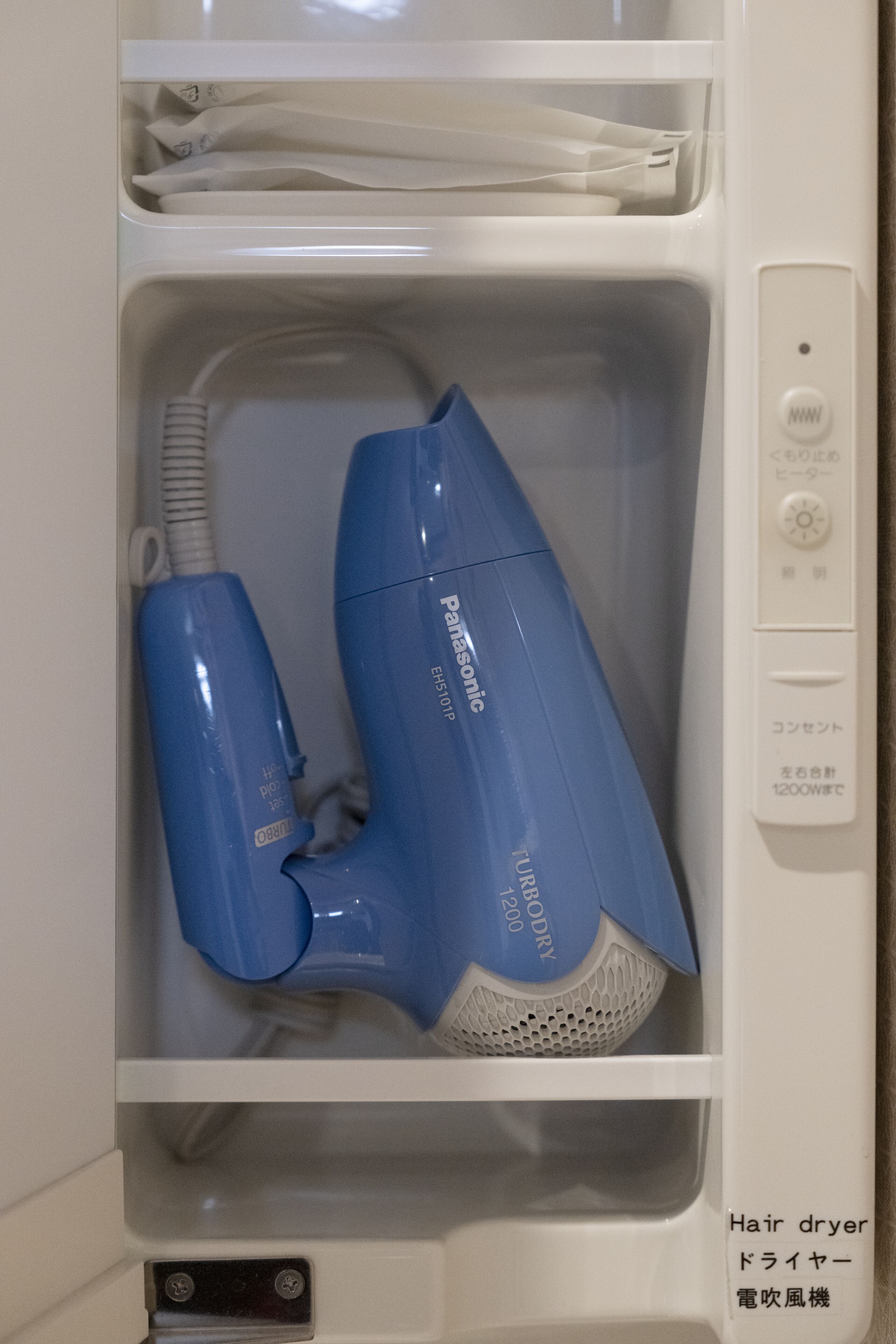 A hair dryer and a smaller appliance in a white cabinet, with Japanese text and a control panel.