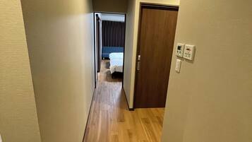 Un couloir étroit, doté d’un plancher en bois, mène à une pièce où se trouvent un lit et une porte.