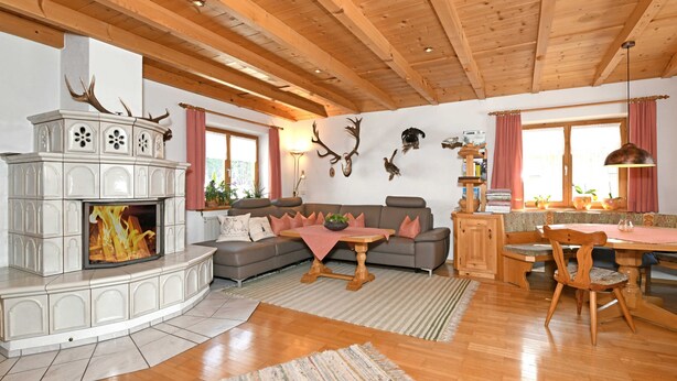 Een woonkamer met een open haard, houten plafond en een eethoek met een tafel en stoelen.