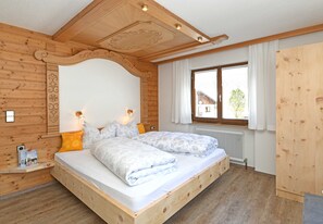 Una habitación de madera con una cama, dos mesitas de noche, un ventanal y un radiador.
