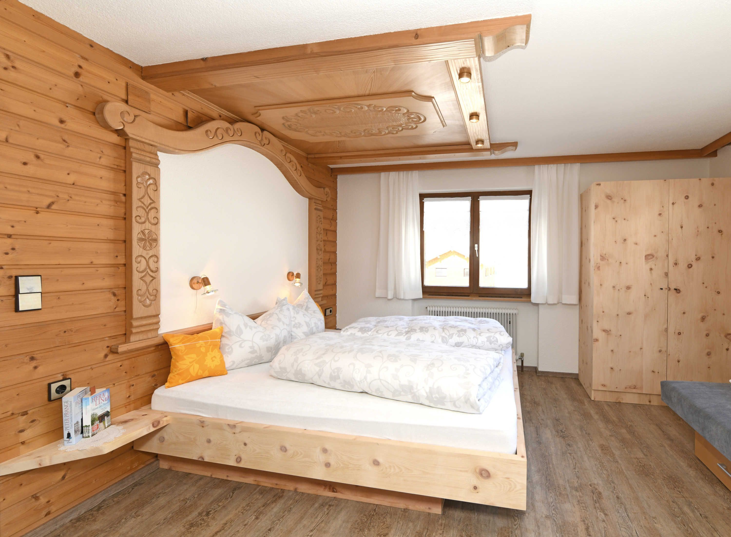 Een slaapkamer met houten vloer, een bed, een raam en een kledingkast.