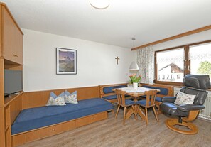 A room with a wooden bench, a dining table with chairs, a television, and a window with curtains.