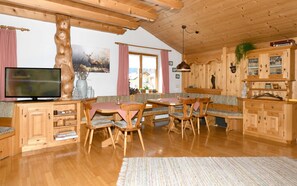 Un interior de madera con una televisión, muebles de madera, una mesa de comedor y un ventanal grande.