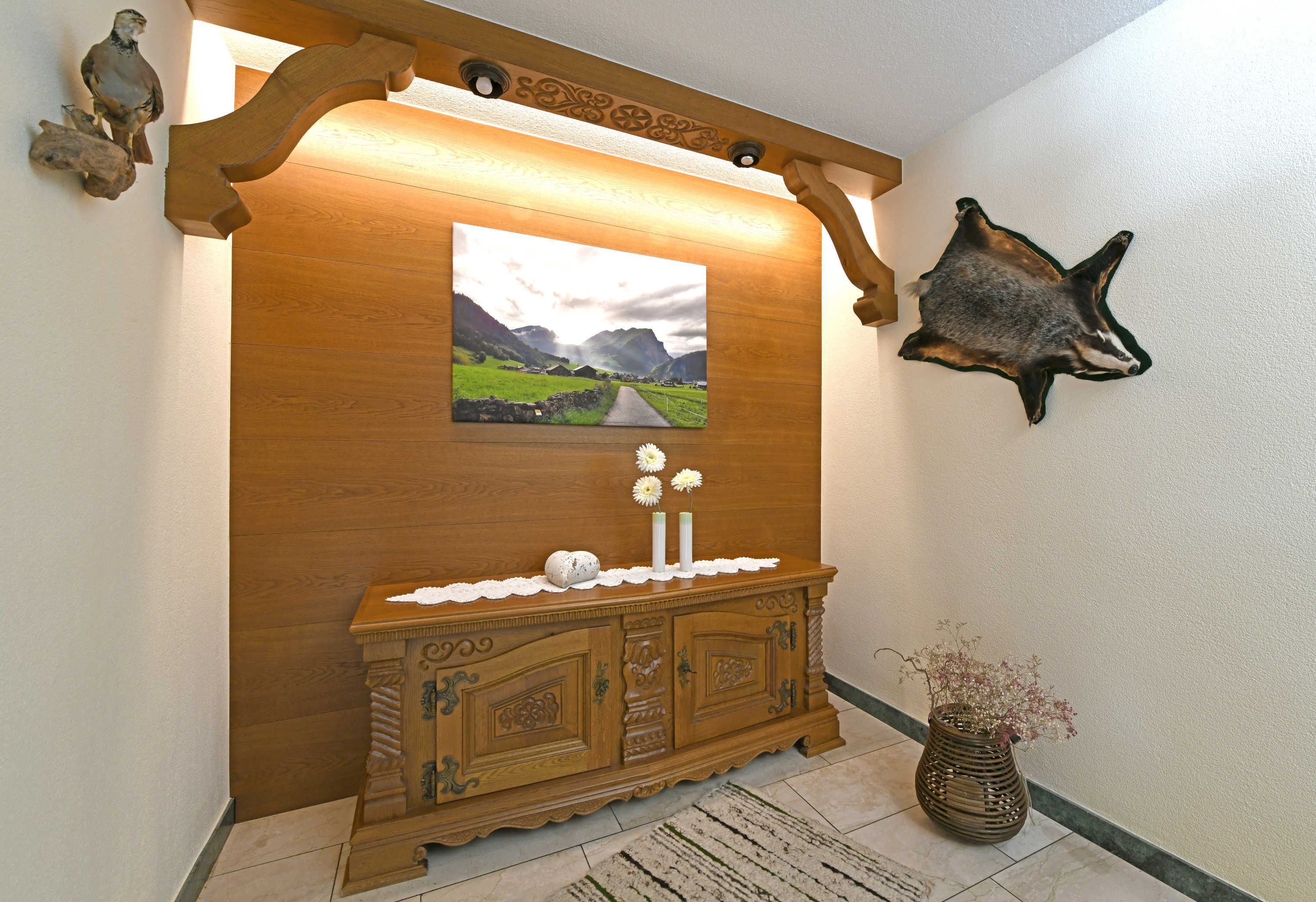 Een houten console met een lijstwerk schilderij van een landschap, een opgeplakt dierenhuid en een vaas met gedroogde bloemen.
