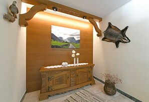Una consola de madera con un cuadro enmarco de un paisaje, un cuero de animal colgado y un jarrón con flores secas.