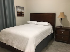 A neatly made bed with white bedding, a wooden headboard, a nightstand with a lamp, and a painting on the wall. - Lake Front House 4BR2B In West Houston (Katy)