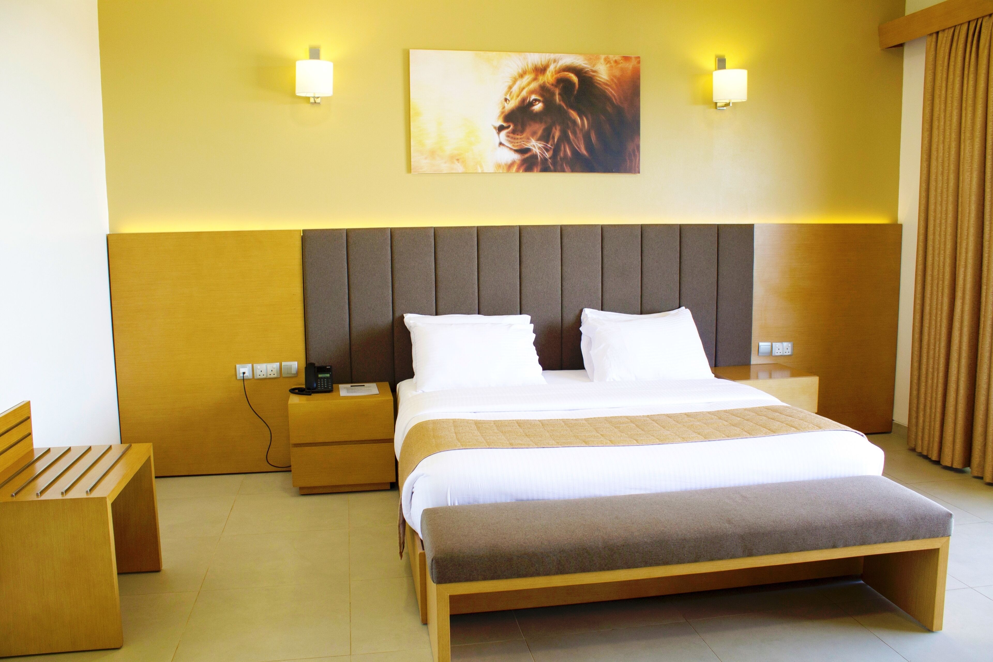 A hotel room with a large bed, bedside tables, a bench, and a wall-mounted picture.