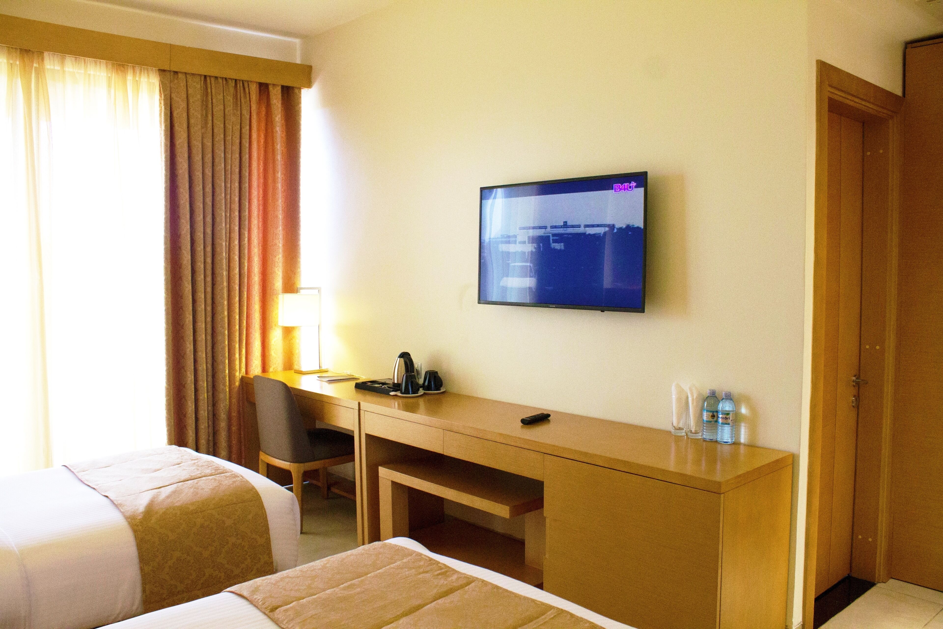 A hotel room with two beds, a desk, a television, and a door.