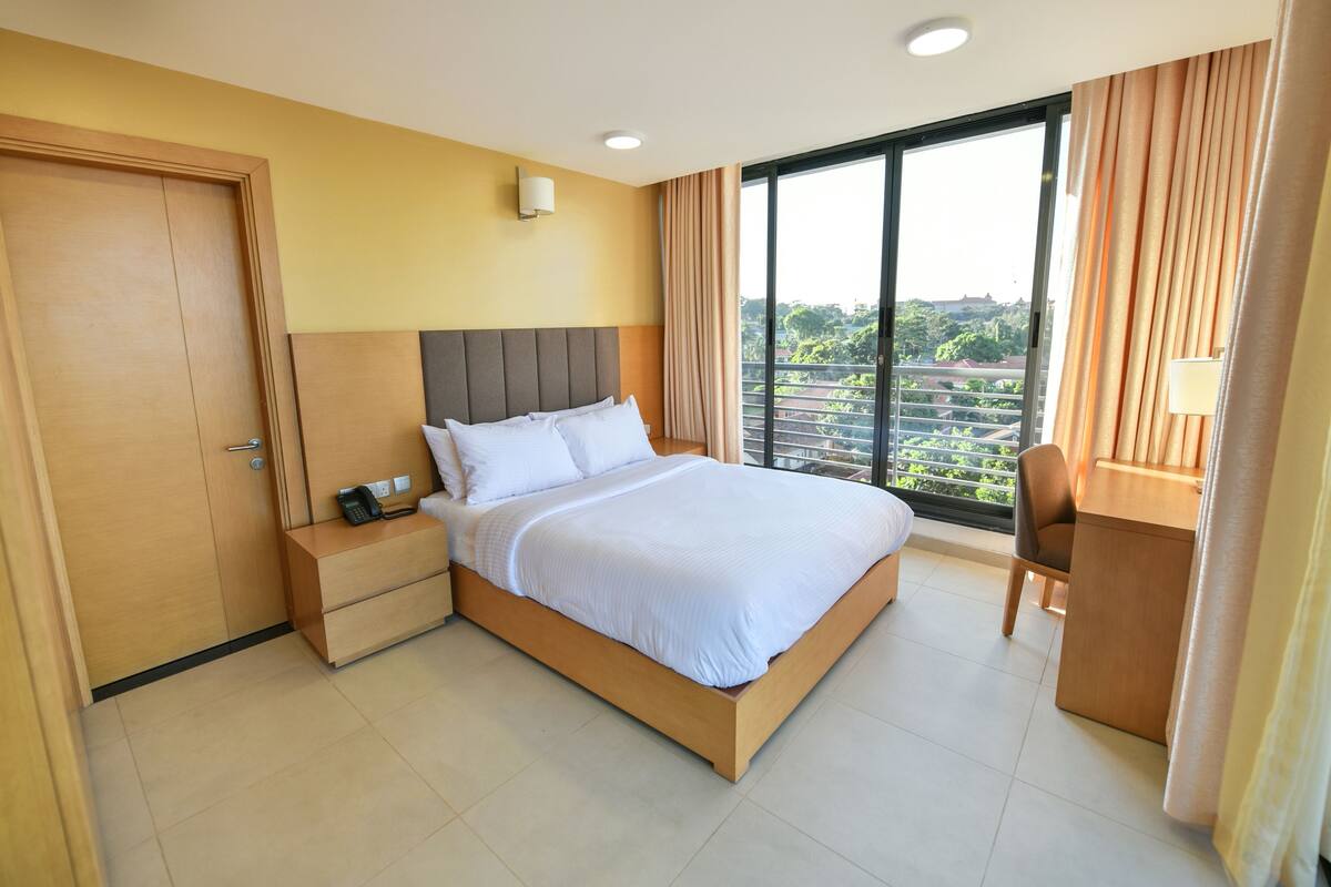 Habitación de hotel con una cama grande, un escritorio y vistas a la vegetación por la ventana.